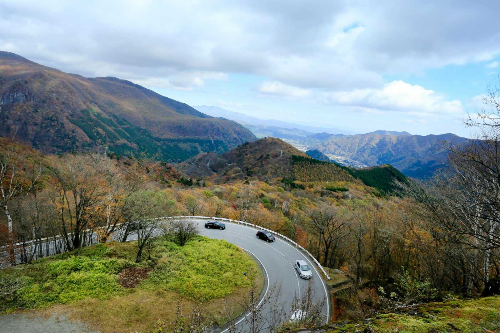 Curved mountain road with cars and stunning fall colors under a cloudy sky.