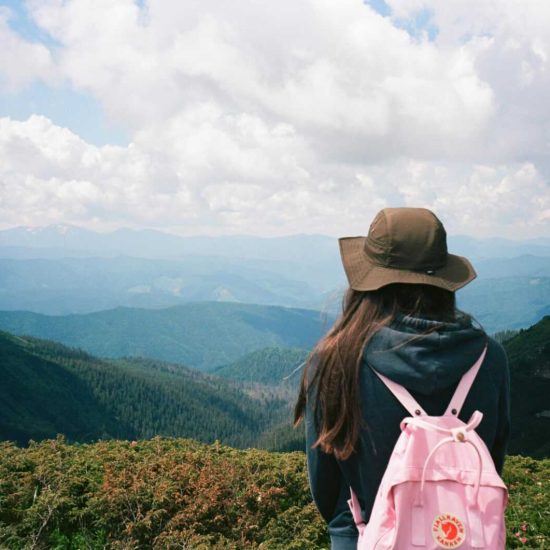 A young woman with a backpack enjoys a stunning mountain view during summer.